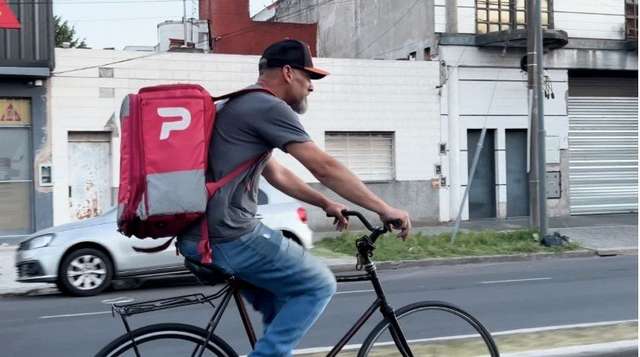 "Un trabajador de pedidos ya andando en bicicleta con la mochila roja grande"