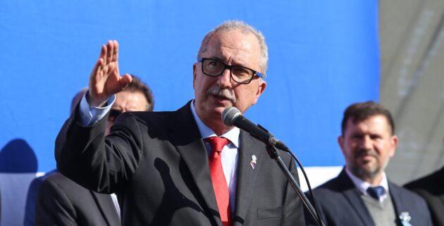 Fotografía del gobernador de Misiones, Hugo Passalacqua, hablando frente a un micrófono durante un acto oficial. Viste traje oscuro y corbata roja, gesticulando con la mano derecha levantada. Fotografía del gobernador de Misiones, Hugo Passalacqua, hablando frente a un micrófono durante un acto oficial. Viste traje oscuro y corbata roja, gesticulando con la mano derecha levantada.