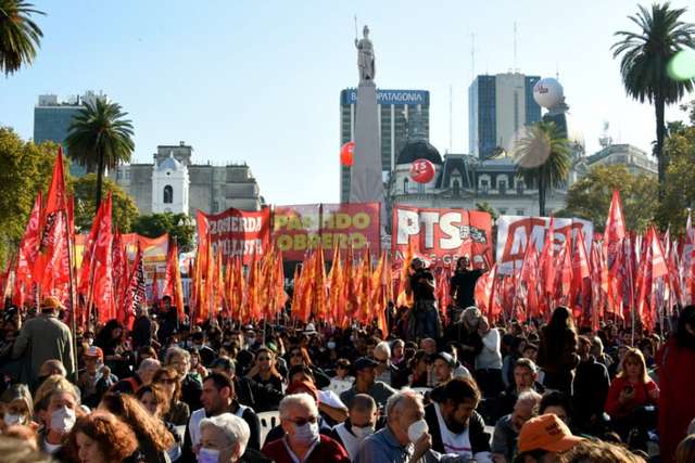 La escena refleja un acto político del Frente de Izquierda Una multitud de personas se encuentra en Plaza de Mayo. Predominan los colores rojo, amarillo y blanco, con numerosas banderas, pancartas y grandes globos rojos flotando sobre el grupo. Se leen letreros con consignas políticas, incluyendo menciones al 'Frente de Izquierda de los Trabajadores', 'Partido Obrero' y 'Izquierda Socialista'.
